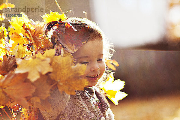 Glückliches Mädchen spielt mit Herbstblättern an einem sonnigen Tag