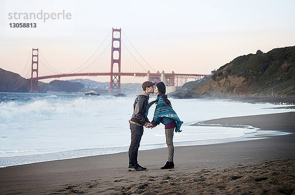 Junges Paar küsst sich am Ufer vor der Golden Gate Bridge
