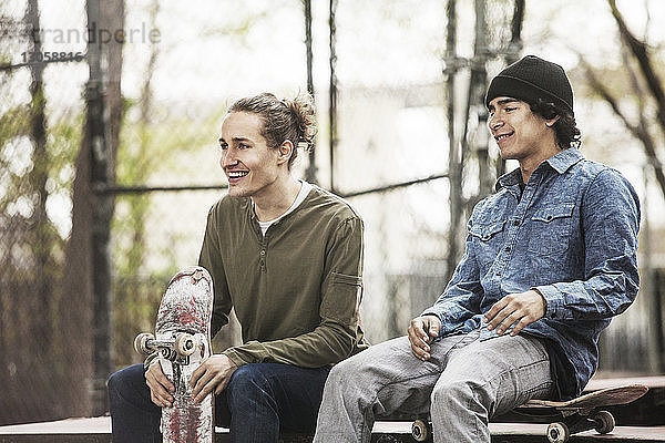 Lächelnde Freunde schauen weg  während sie im Skateboard-Park sitzen
