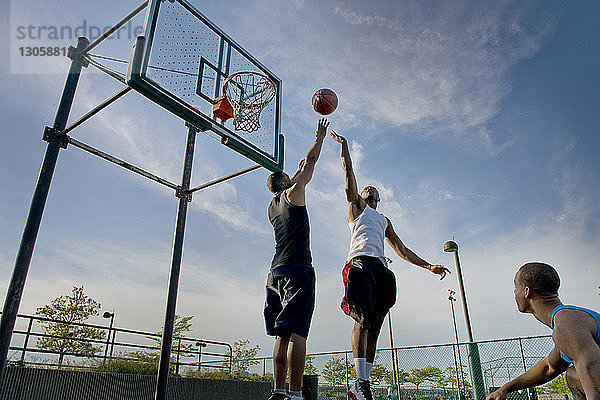 Niedrigwinkelansicht von Sportlern  die Basketball vor Gericht gegen den Himmel spielen