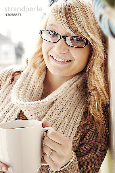 Fröhliche Frau hält Kaffeetasse  während sie an der Wand lehnt