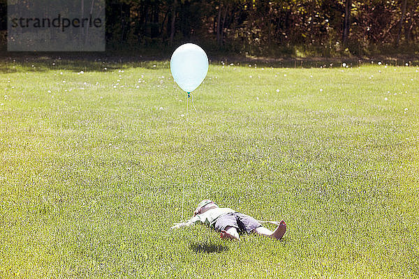 Auf Grasfeld liegender Junge mit Ballon