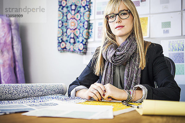 Porträt einer selbstbewussten Modedesignerin  die beim Workshop am Schreibtisch sitzt