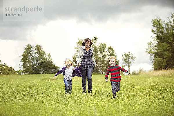 Glückliche Mutter geht mit Kindern auf Grasfeld gegen den Himmel