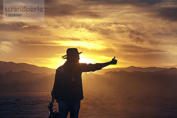 Silhouette eines Mannes mit Daumen bei Sonnenuntergang
