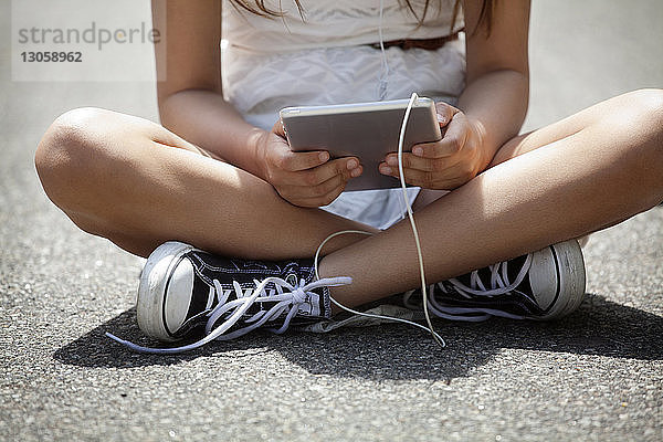 Unterer Teil eines Mädchens hält Tablette  während es auf der Straße sitzt