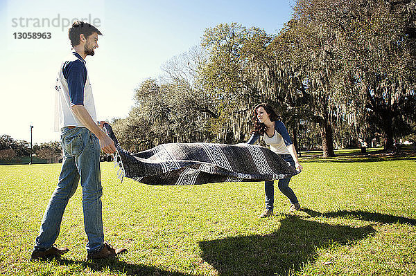 Paar  das während eines sonnigen Tages eine Decke auf dem Feld im Park ausbreitet