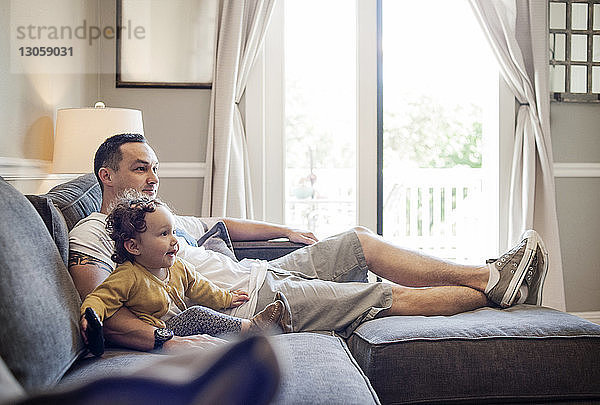 Vater und Tochter schauen fern  während sie zu Hause auf dem Sofa sitzen
