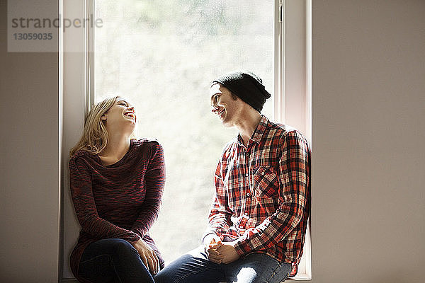 Fröhliches Paar unterhält sich auf der Fensterbank sitzend