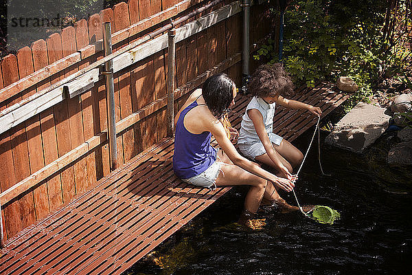 Mutter und Tochter sitzen auf der Fußgängerbrücke über den Teich im Hinterhof