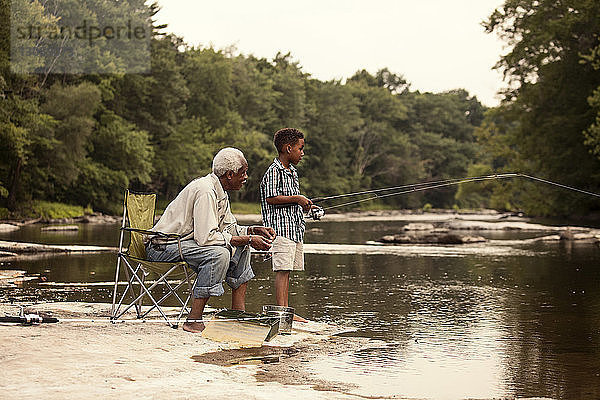 Großvater schaut seinem Enkel beim Angeln zu  während er am See sitzt