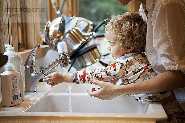 Ausgeschnittenes Bild einer Mutter  die ihrem Sohn beim Händewaschen an der Küchenspüle hilft