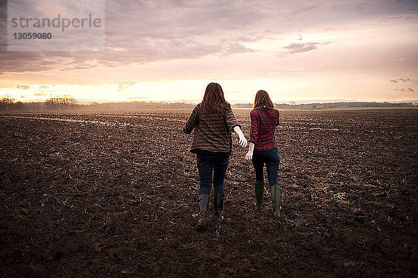 Rückansicht von Freundinnen  die bei Sonnenaufgang auf dem Feld gegen den Himmel laufen