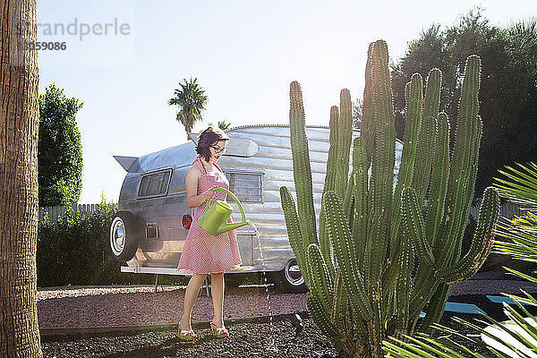 Frau gießt Kaktus in voller Länge  während sie gegen ein Wohnmobil steht