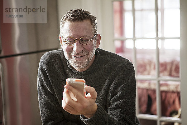 Lächelnder Mann benutzt Smartphone zu Hause