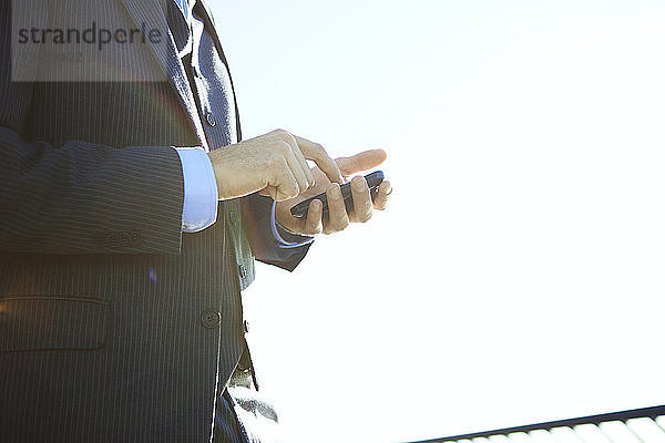 Seitenansicht eines Geschäftsmannes mit einem Smartphone bei klarem Himmel