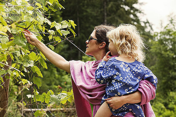 Frau sammelt Blätter  während sie ein Mädchen aufs Feld trägt