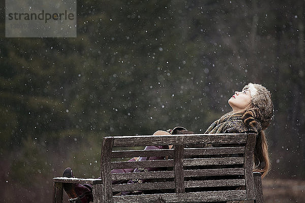 Nachdenkliche Frau schaut auf  während sie sich auf einer Bank im Wald entspannt