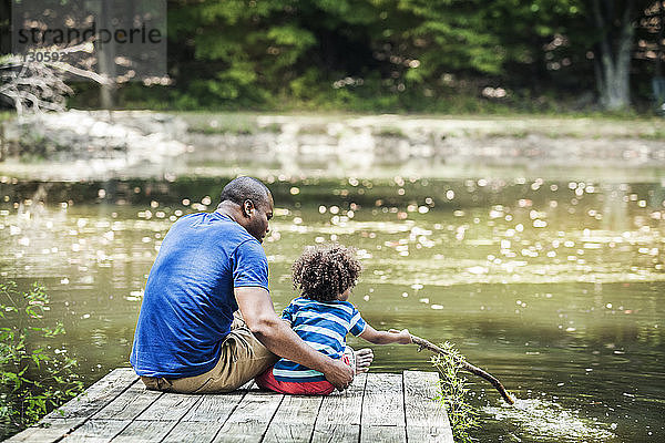 Vater betrachtet Sohn beim Spielen mit Stock am See