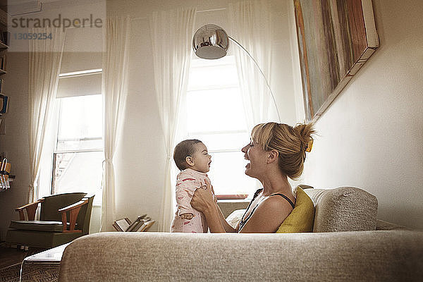 Seitenansicht einer Mutter  die mit ihrer Tochter spielt  während sie zu Hause auf dem Sofa sitzt