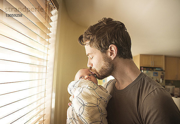 Vater küsst Baby-Tochter am Fenster zu Hause
