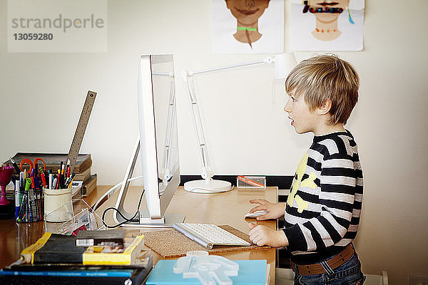 Seitenansicht eines Jungen  der zu Hause einen Desktop-Computer benutzt