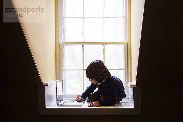 Junge benutzt Laptop-Computer  während er sich zu Hause auf den Boden lehnt