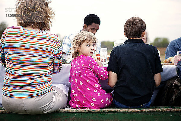 Porträt eines Mädchens  das mit Familie und Freunden am Picknicktisch sitzt