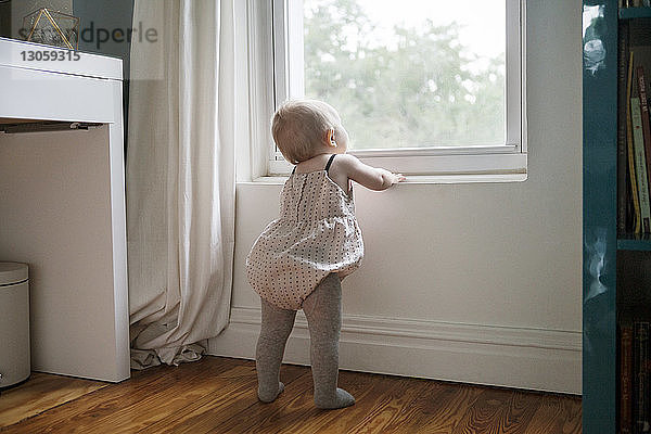 Rückansicht eines Mädchens  das durch ein Fenster schaut