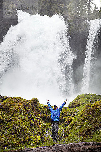 Glücklicher Mann steht am Wasserfall am Wald