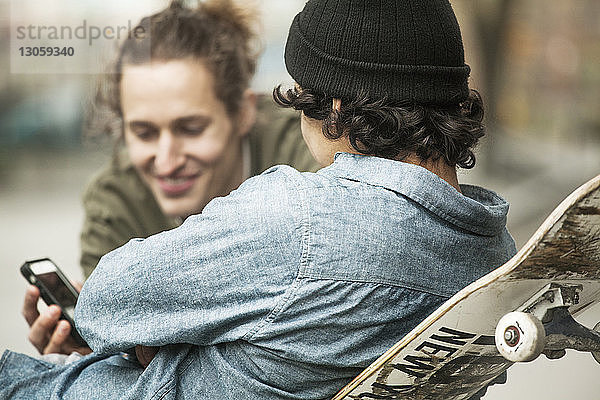 Freunde schauen beim Entspannen im Skateboard-Park aufs Handy