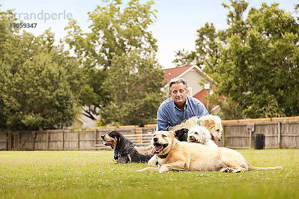 Porträt eines Mannes  der mit Hunden auf einem Grasfeld im Hof sitzt