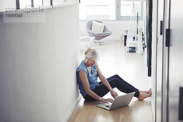 Ältere Frau sitzt auf dem Boden und benutzt zu Hause einen Laptop