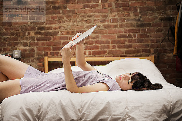 Junge Frau liegt auf dem Bett und benutzt zu Hause ein digitales Tablett