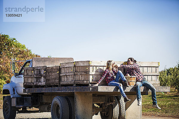 Mann teilt Obst mit seiner Freundin  während er auf einem Lastwagen vor klarem Himmel sitzt