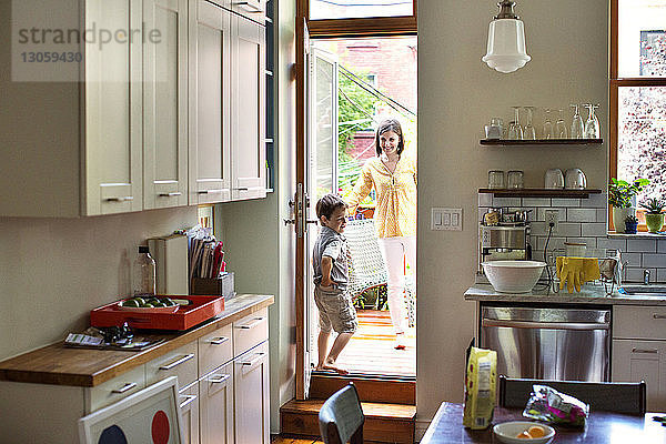 Glückliche Mutter betrachtet Sohn durch Küchentür gesehen