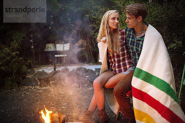 Romantisches Paar in eine Decke gehüllt am Lagerfeuer sitzend