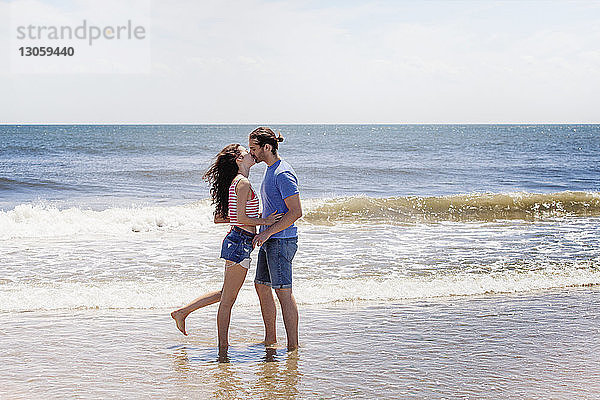 Zärtliches Paar küsst sich  während es am Strand am Ufer steht