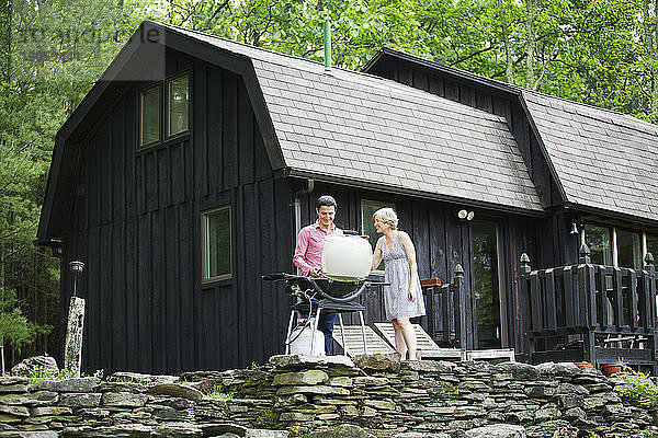 Ehepaar bereitet Essen auf dem Grill vor  während es an der Hütte steht