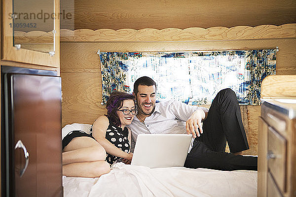 Lächelndes Paar benutzt Laptop-Computer  während es im Wohnmobil im Bett sitzt