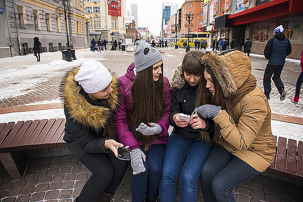 Freunde telefonieren  während sie im Winter auf der Bank sitzen