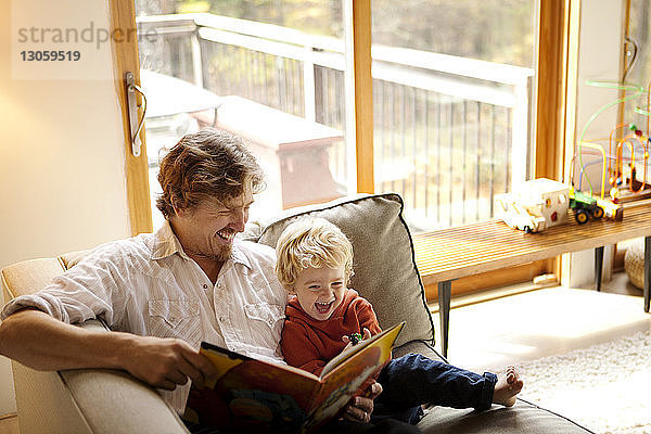 Vater liest mit dem Sohn ein Buch  während er zu Hause auf dem Sofa sitzt