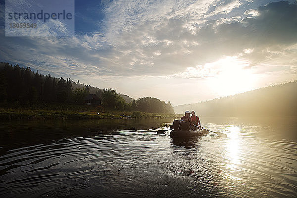 Mann und Frau beim River-Rafting bei Sonnenuntergang