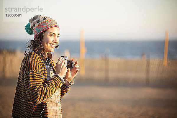 Fröhliche Frau mit Digitalkamera am Strand stehend
