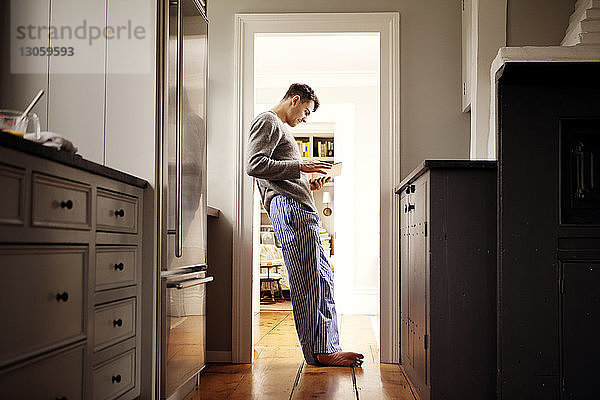 Seitenansicht eines Mannes  der eine Tablette benutzt  während er sich zu Hause an die Tür lehnt