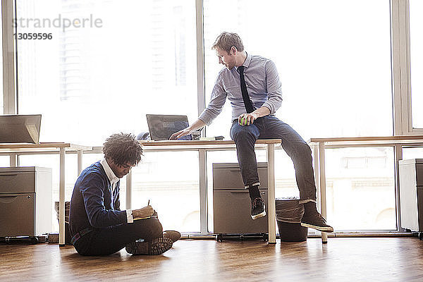 Geschäftsmann benutzt Laptop  während ein Kollege im Büro sitzt