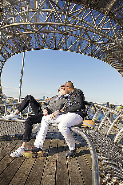Freunde küssen sich  während sie auf einem Metallsitz sitzen