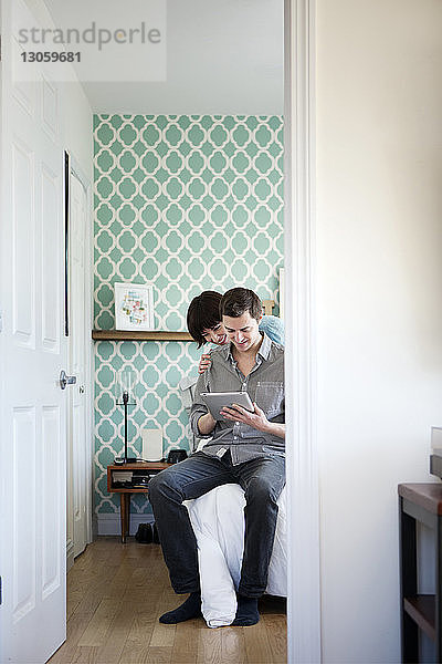 Glückliches Paar betrachtet Tablet-Computer  während es zu Hause im Bett sitzt