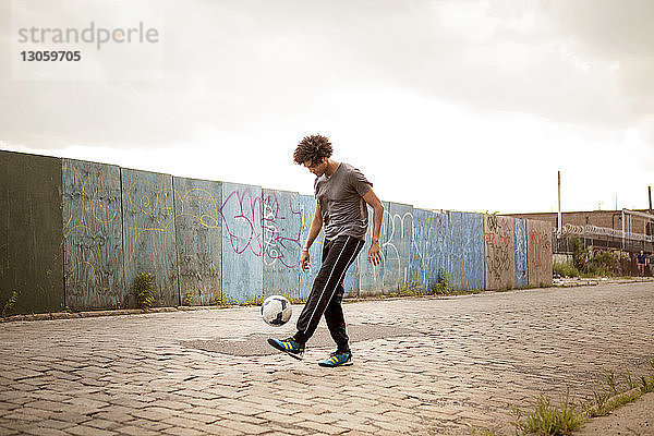 Mann jongliert Fußball auf Fußpfad