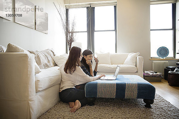 Freundinnen  die einen Laptop benutzen  während sie zu Hause auf einem Teppich sitzen